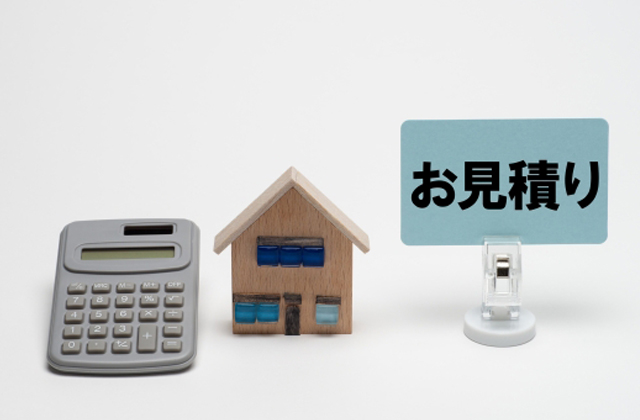 電卓と家の模型と見積もりと書かれたメモ