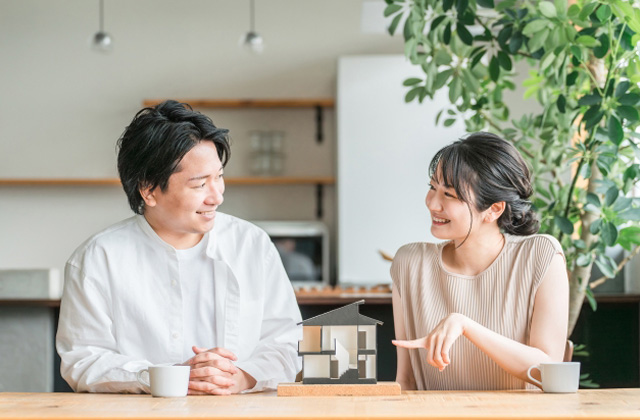 家の模型をはさんで話している夫婦