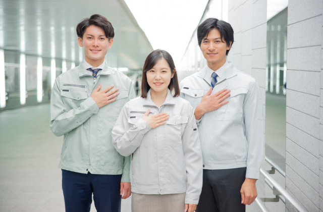 胸に手を当てた作業服を着ている男女3人